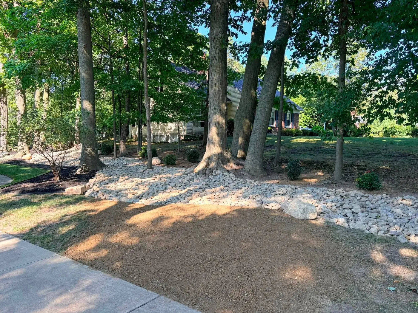 Wooded landscape bed finished with white decorative stone beside a walkway, a Stone Mountain Lawn Care job